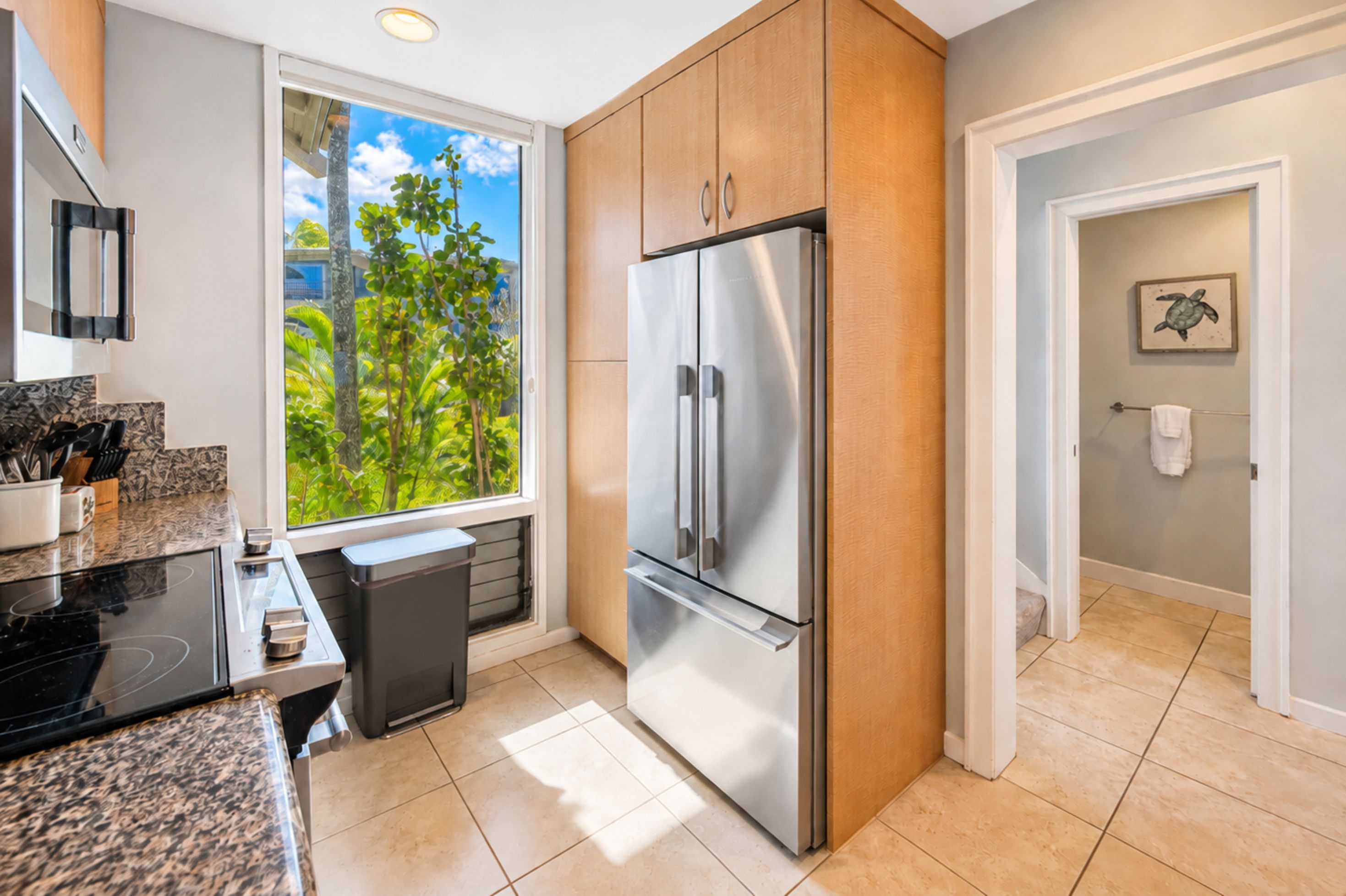 A modern kitchen with a stainless steel refrigerator, a window with a view of greenery, and a countertop with kitchen utensils.