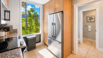A modern kitchen with a stainless steel refrigerator, a window with a view of greenery, and a countertop with kitchen utensils.