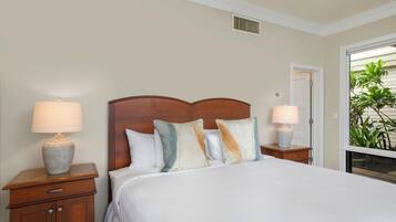 A hotel room with a large bed, two bedside tables with lamps, a wooden headboard, and a view of greenery outside.