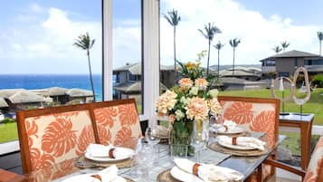 A dining table set for four with a view of the ocean and palm trees.