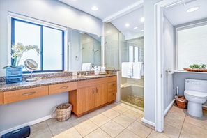 Un baño moderno con un espejo grande, encimera de granito, armarios de madera y una cabina de ducha de vidrio.