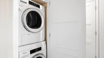 A stacked washer and dryer unit in a white-walled room with a closed door.