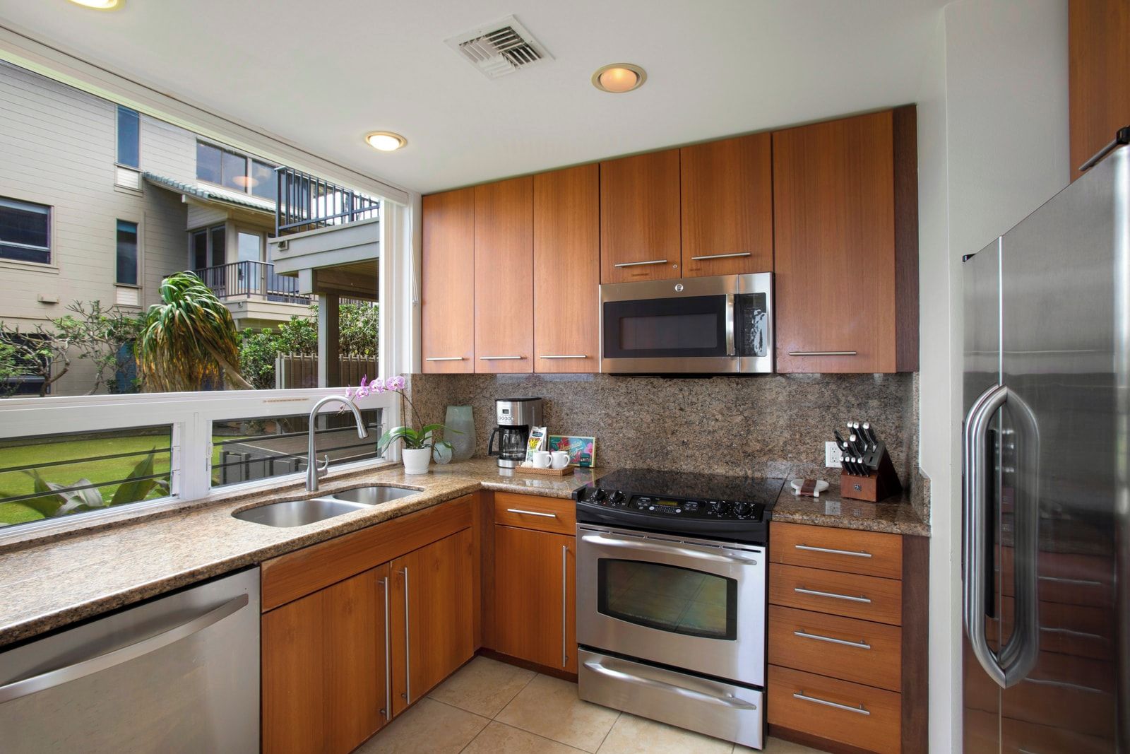 A modern kitchen with stainless steel appliances, wooden cabinets, and a window overlooking a balcony.