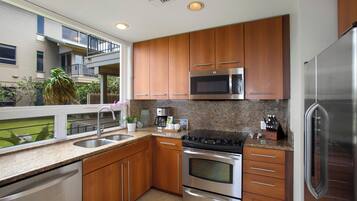 A modern kitchen with stainless steel appliances, wooden cabinets, and a window overlooking a balcony.