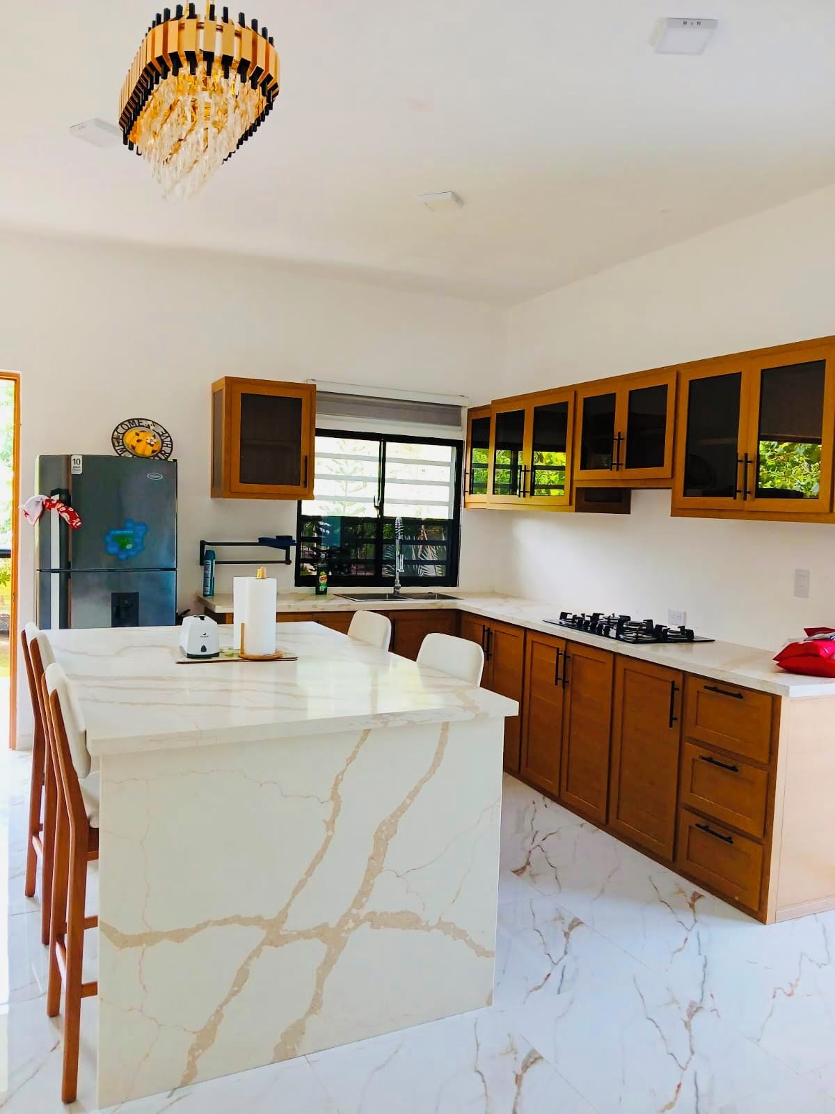 A modern kitchen with a marble island, wooden cabinets, and a built-in gas stove.