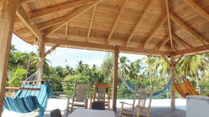 A wooden structure with a thatched roof, outdoor seating with chairs and hammocks, and a view of palm trees. - Santa Capuza 2 (Sánchez  las garitas)