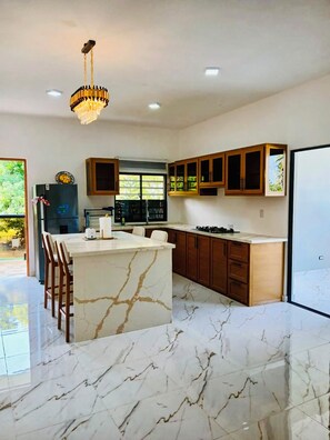 A modern kitchen with a marble island, wooden cabinets, and a chandelier.