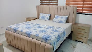 A bedroom with a bed, two nightstands, a wooden headboard, and a window with blinds.