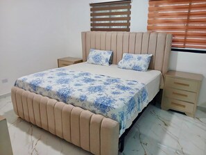 A bedroom with a bed, two nightstands, a wooden headboard, and a window with blinds.