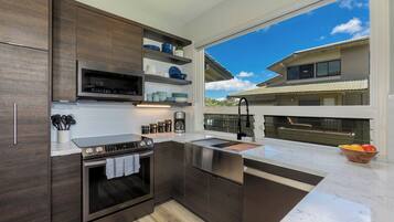 A modern kitchen with dark wood cabinets, stainless steel appliances, and a large window offering a view of a residential building.