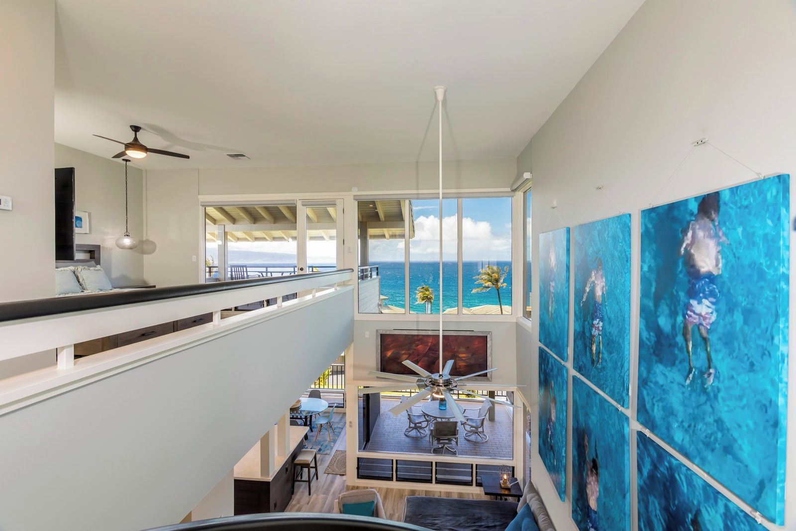A multi-level interior with a balcony overlooking the ocean, a dining area, and artwork on the walls.