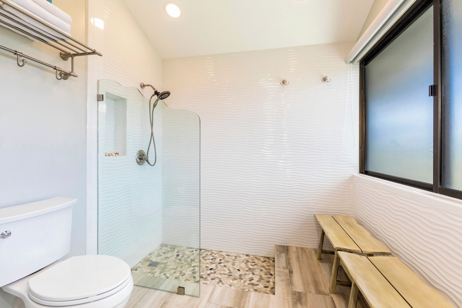 Un baño con cabina de ducha de vidrio, inodoro y banco.