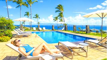 A poolside area with lounge chairs, umbrellas, and a view of the ocean.