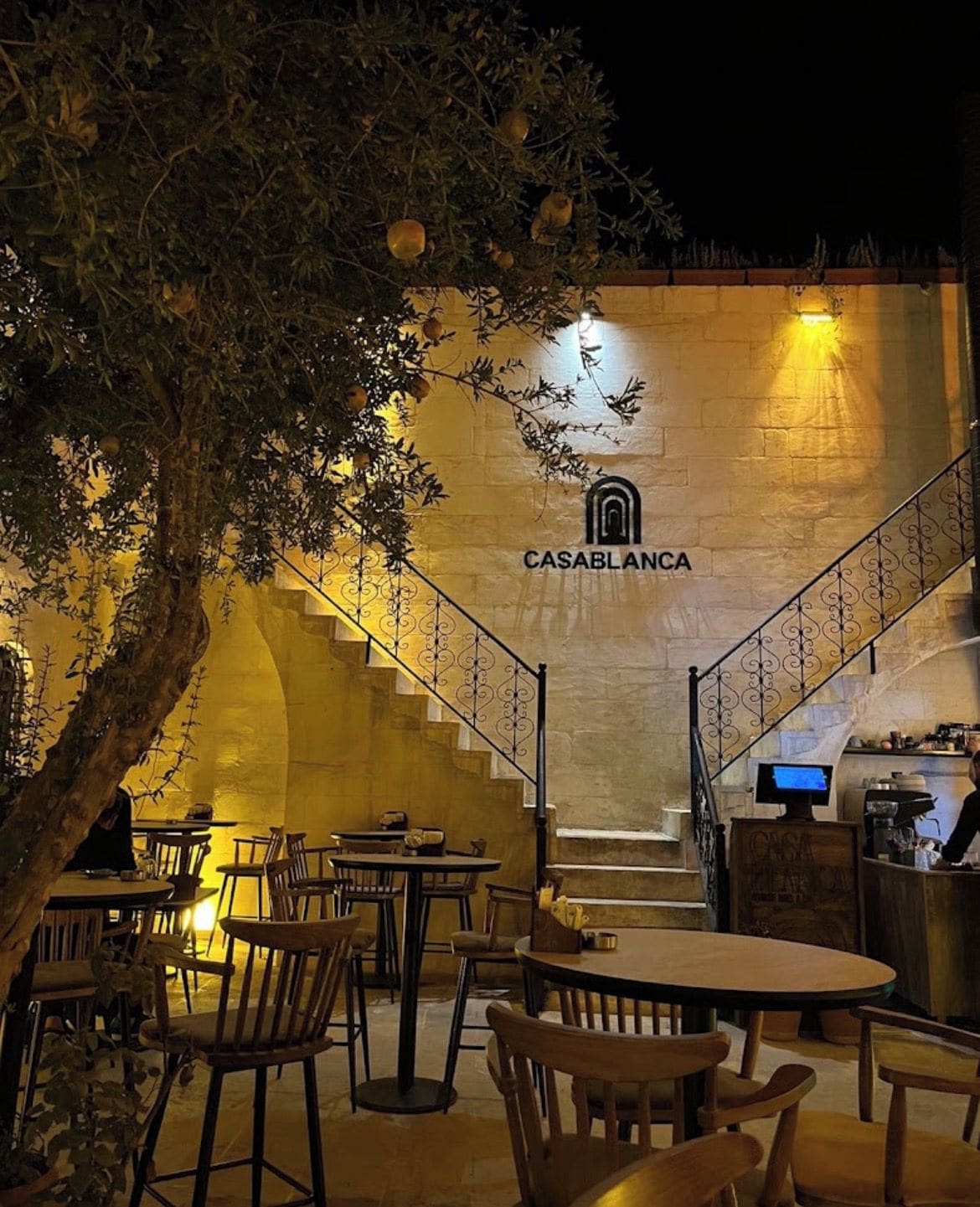 Área externa com mesas e cadeiras, escada que leva a um andar superior e uma parede com a placa 'CASABLANCA'.