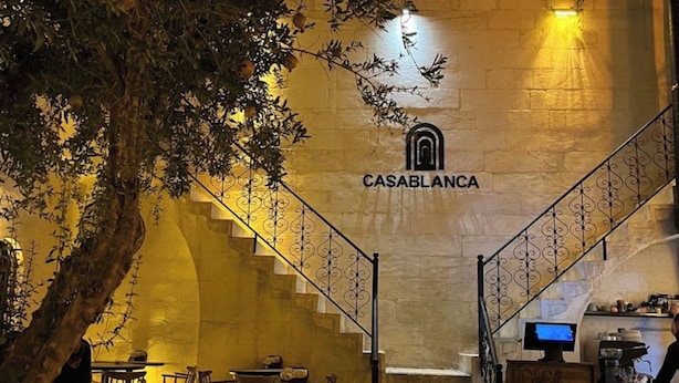 An outdoor seating area with tables and chairs, a staircase leading to an upper level, and a wall with the 'CASABLANCA' sign. - Casa Blanca otel (Şanlıurfa)