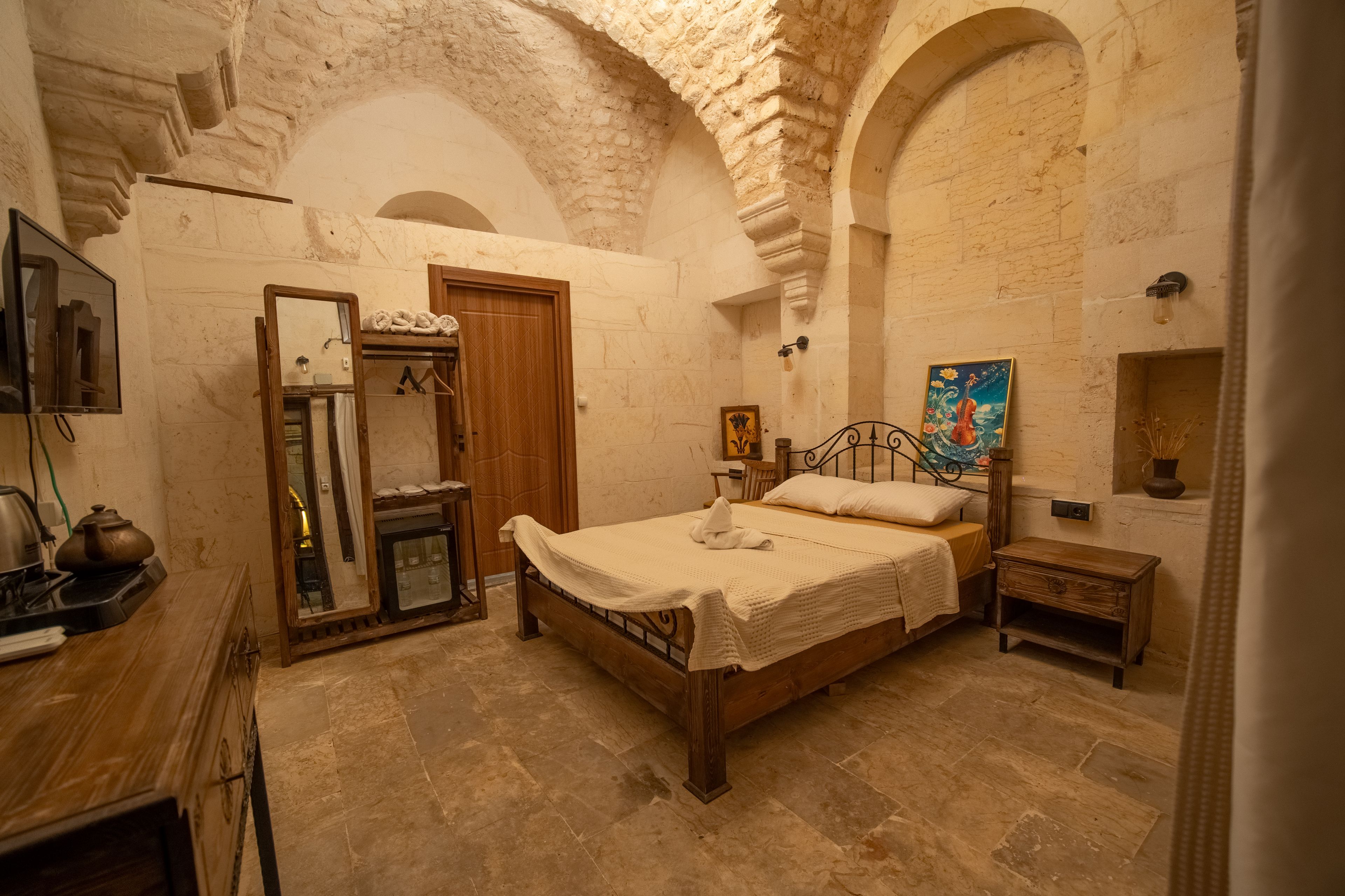 Quarto com cama, guarda-roupa de madeira, espelho, mesa pequena e um quadro na parede.