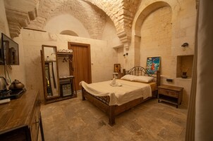 Una habitación con cama, armario de madera, espejo, una mesita y un cuadro en la pared.