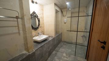 A bathroom with a sink, mirror, shower, and a wooden door.