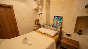 A room with a bed, a wooden nightstand, a painting, and a small table with a vase. - Casa Blanca otel (Şanlıurfa)