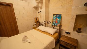 A room with a bed, a wooden nightstand, a painting, and a small table with a vase.