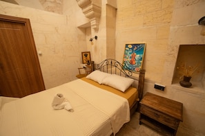 Quarto com cama, mesa de cabeceira de madeira, um quadro e uma pequena mesa com um vaso.