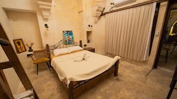 Un dormitorio con cama, una silla, un cuadro y una ventana con cortinas.