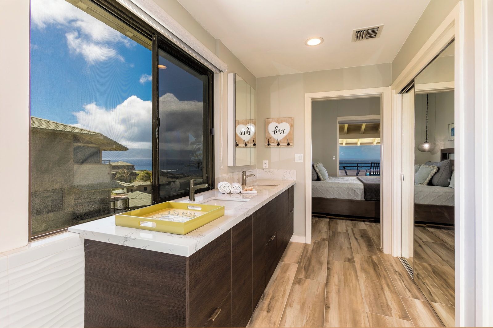 A modern bathroom with a large window, a vanity with a marble countertop, and a view of the ocean.