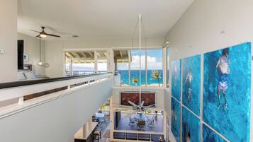 A multi-level interior with a balcony overlooking the ocean, a dining area, and artwork on the walls.