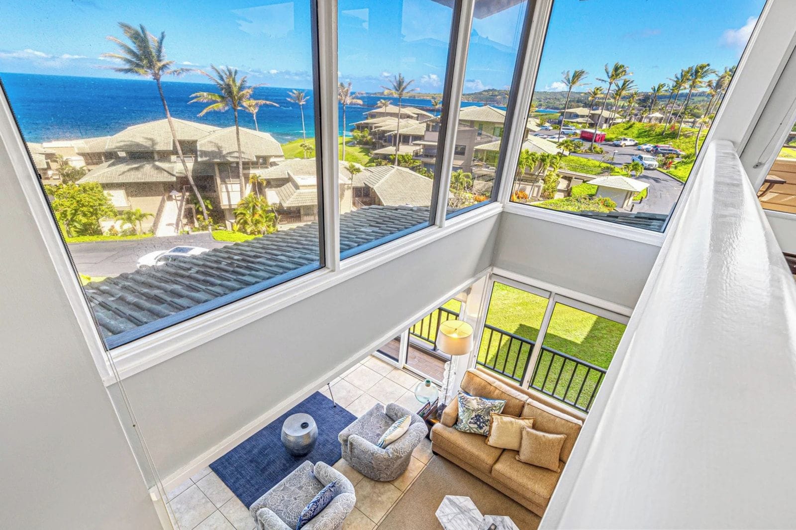 Et værelseshotel i højhus med balkon og udsigt over kysten, med sofa, lampe og havudsigt samt palmer.