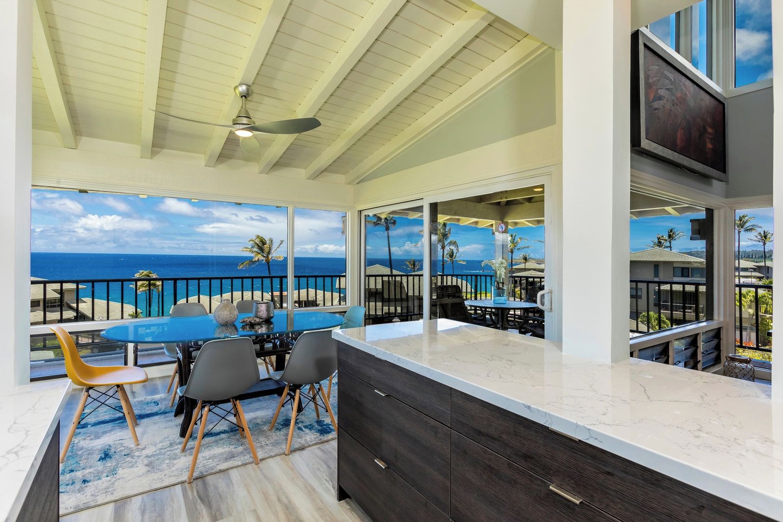 A modern kitchen with a large island, a dining area with a view of the ocean, and a ceiling fan.