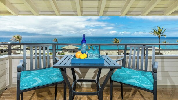 Een balkon met een tafel, stoelen en uitzicht op de oceaan.
