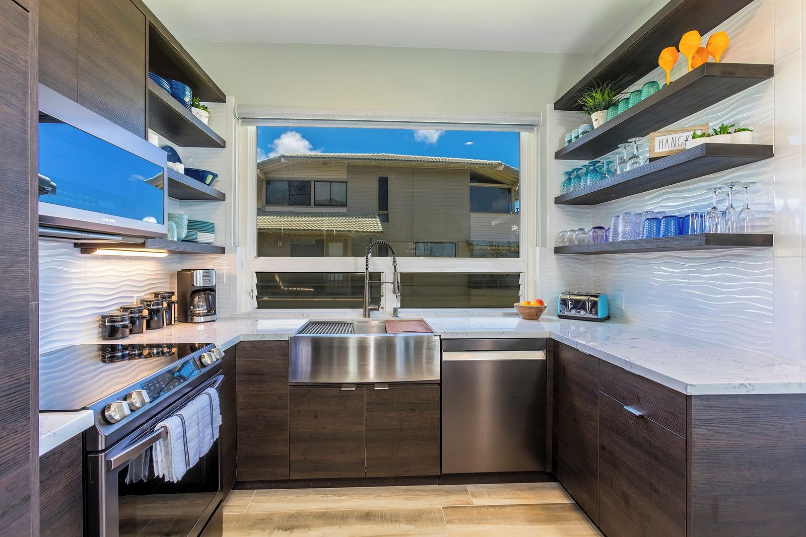 Une cuisine moderne avec des meubles en bois foncé, des appareils électroménagers en acier inoxydable et une fenêtre donnant sur un immeuble.