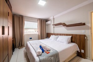 A hotel room with a bed, curtains, a window, an air conditioning unit, and a wooden headboard. - Charming Apt w/ Air Conditioning in Pituba Gaa0103 (Salvador)