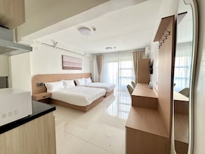 Quarto de hotel com cozinha compacta, duas camas, escrivaninha e televisão.