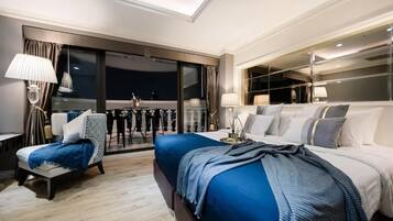 Habitación de hotel moderna con una cama grande, una zona de estar con una silla y una mesa, y un balcón con vistas.