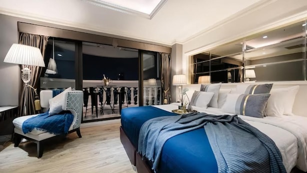 A modern hotel room with a large bed, a seating area with a chair and a table, and a balcony with a view. - State Tower Bangkok (Krung Thep Maha Nakhon)