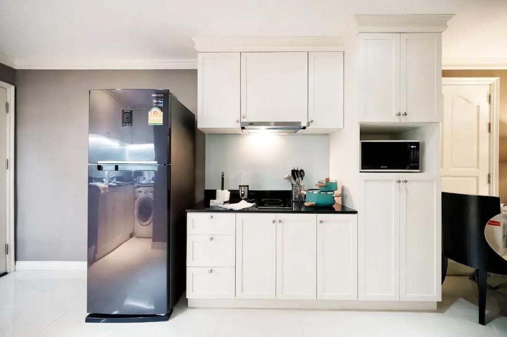Cocina compacta con gabinetes blancos, microondas integrado y refrigerador de acero inoxidable.