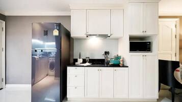 Cocina compacta con gabinetes blancos, microondas integrado y refrigerador de acero inoxidable.