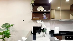 A modern kitchen with a black countertop, white chairs, and a potted plant. - State Tower Bangkok (Krung Thep Maha Nakhon)