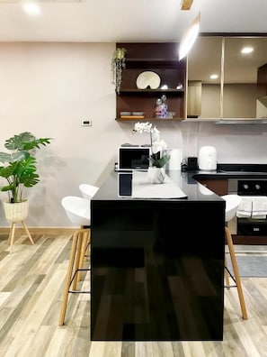 Una cocina moderna con encimera negra, sillas blancas y una planta en maceta.