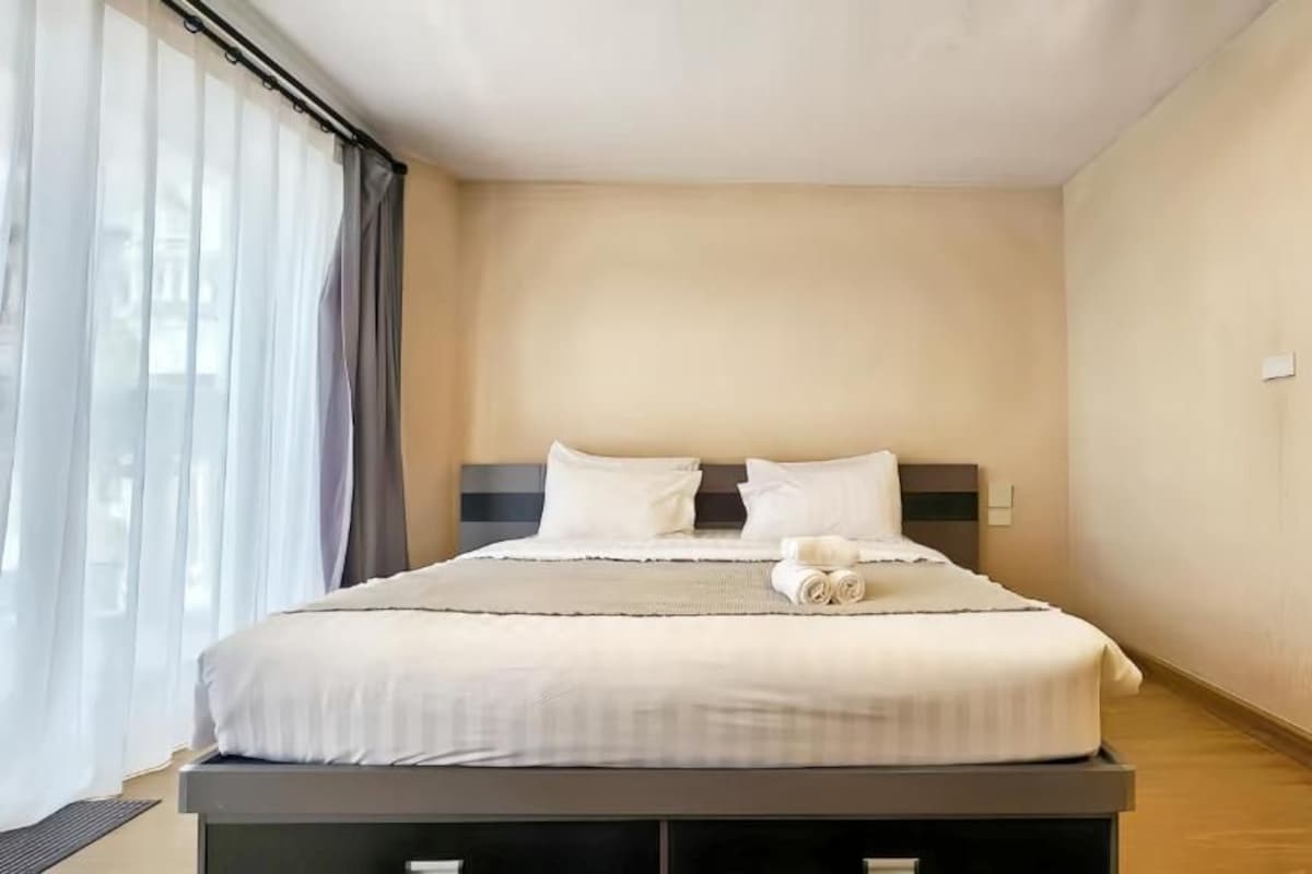 Una habitación de hotel con cama, ventana con cortinas y mesita de noche.