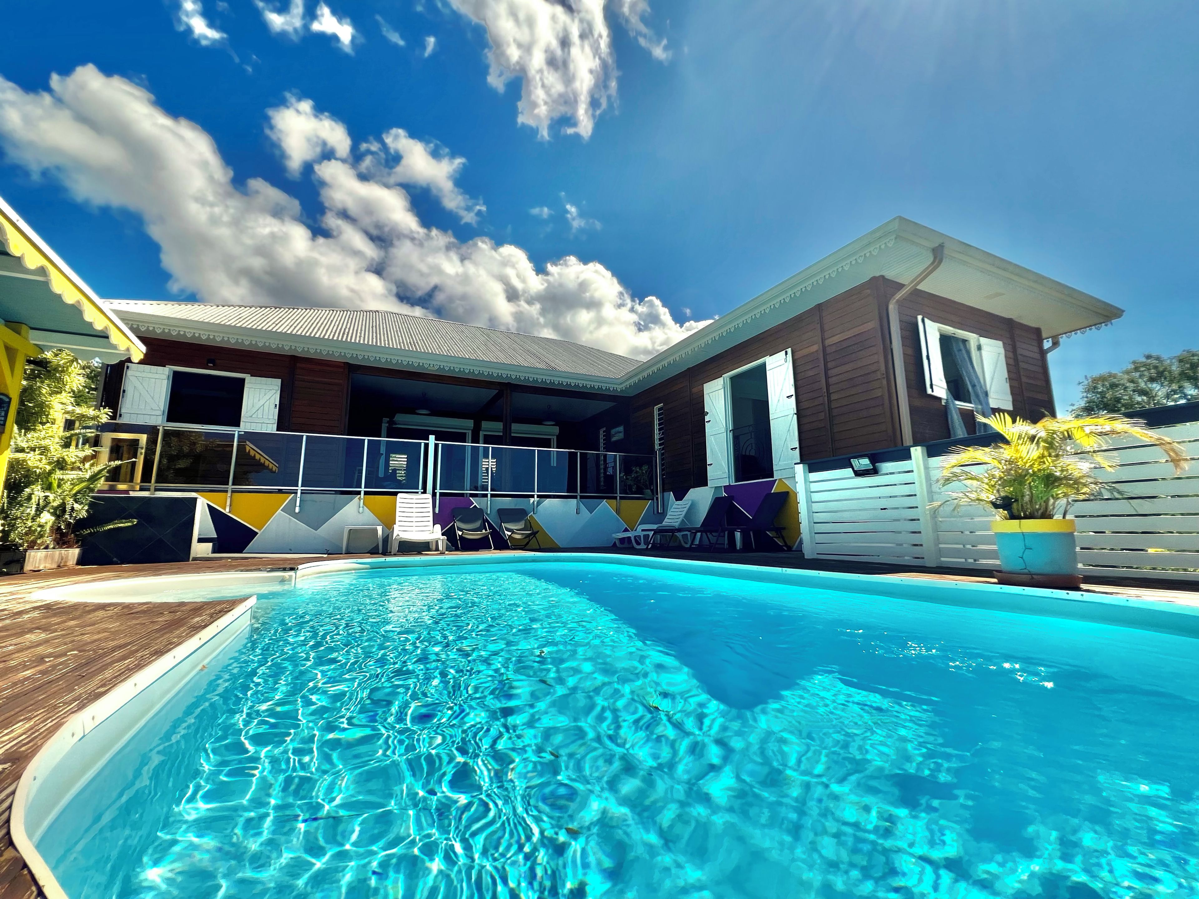 A swimming pool with lounge chairs, a wooden deck, and a building with a balcony.