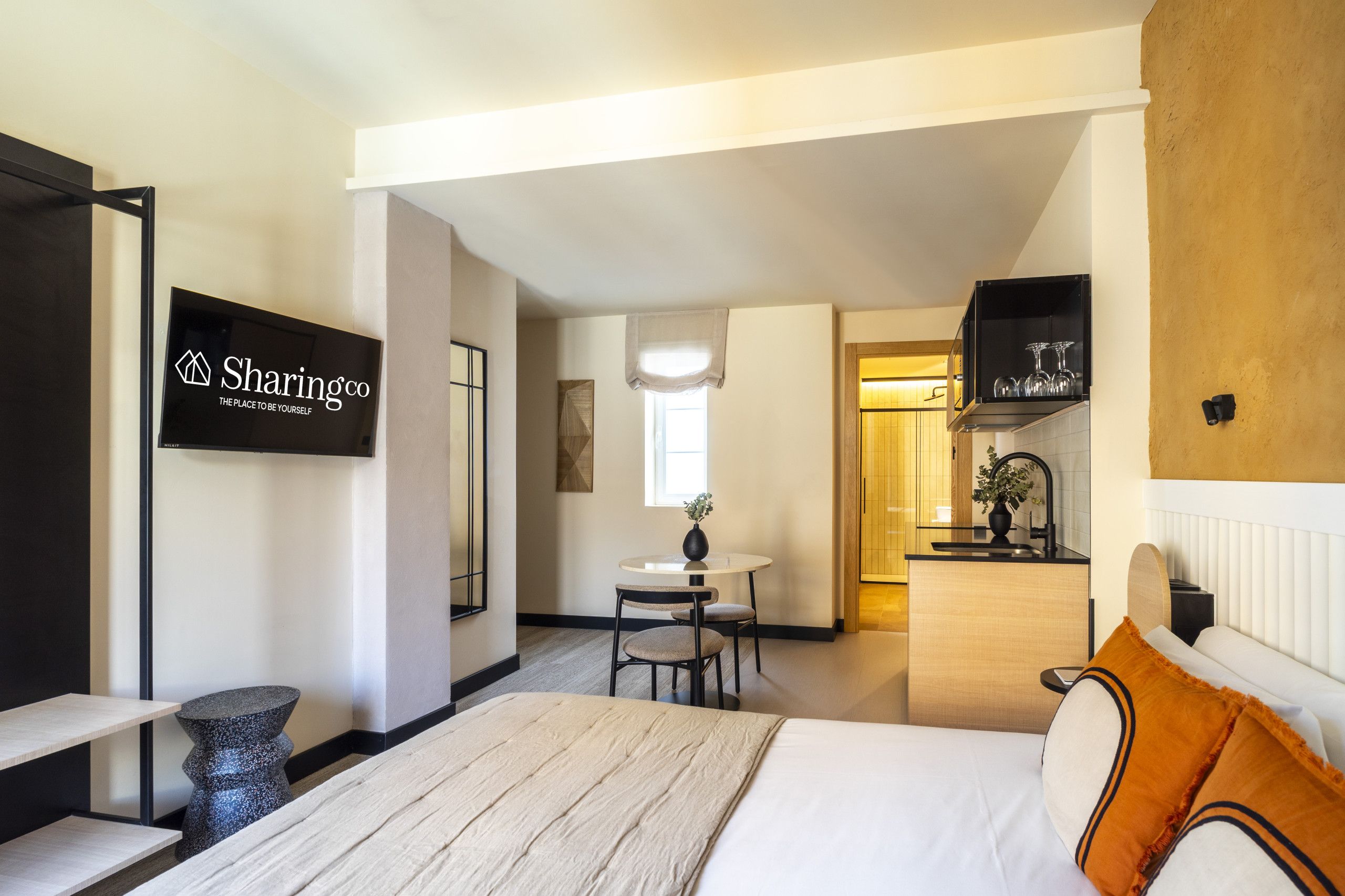 A hotel room with a bed, a desk, a chair, a small table, and a television mounted on the wall.
