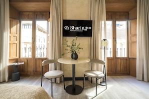 Una habitación con una mesa redonda, dos sillas, un televisor en la pared y una ventana con cortinas.