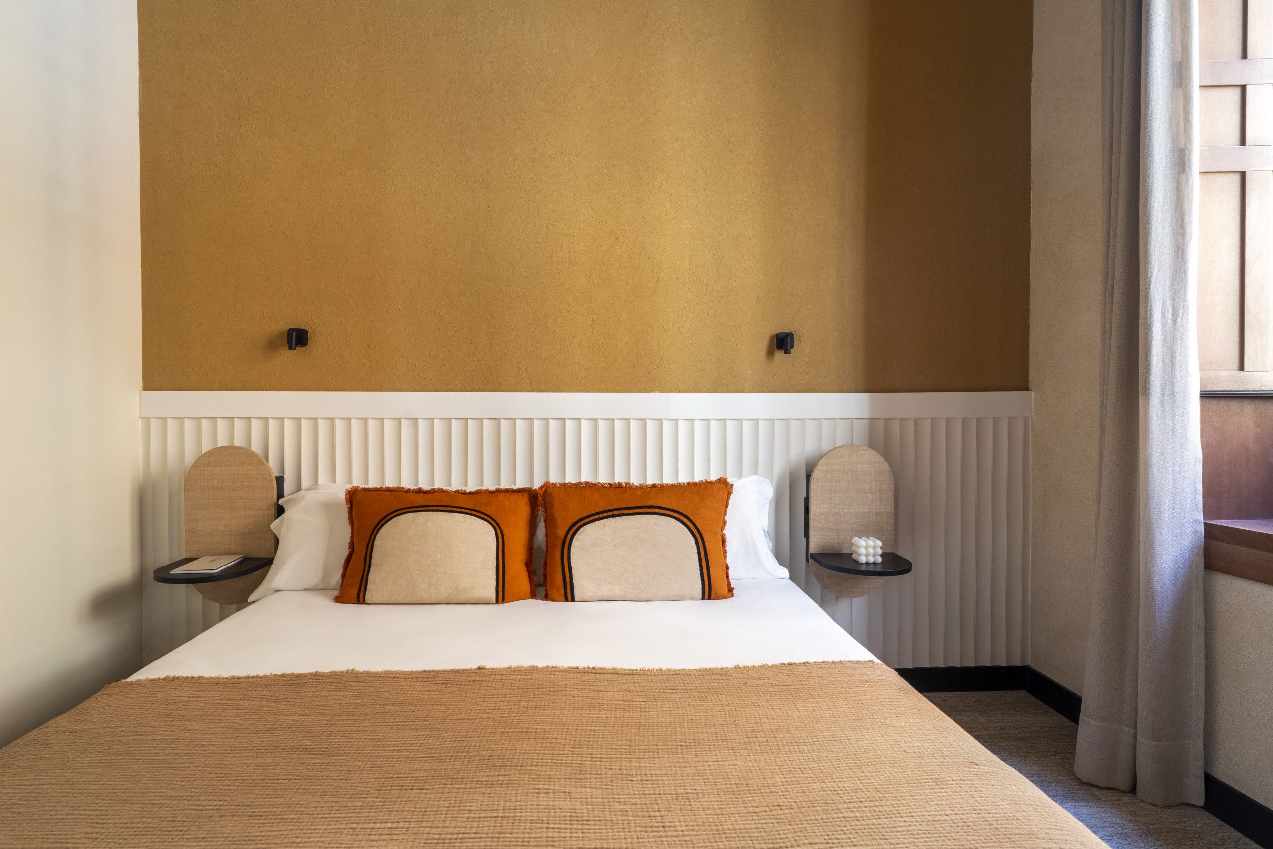 Una habitación de hotel con una cama grande, dos mesitas de noche y una ventana con cortinas.