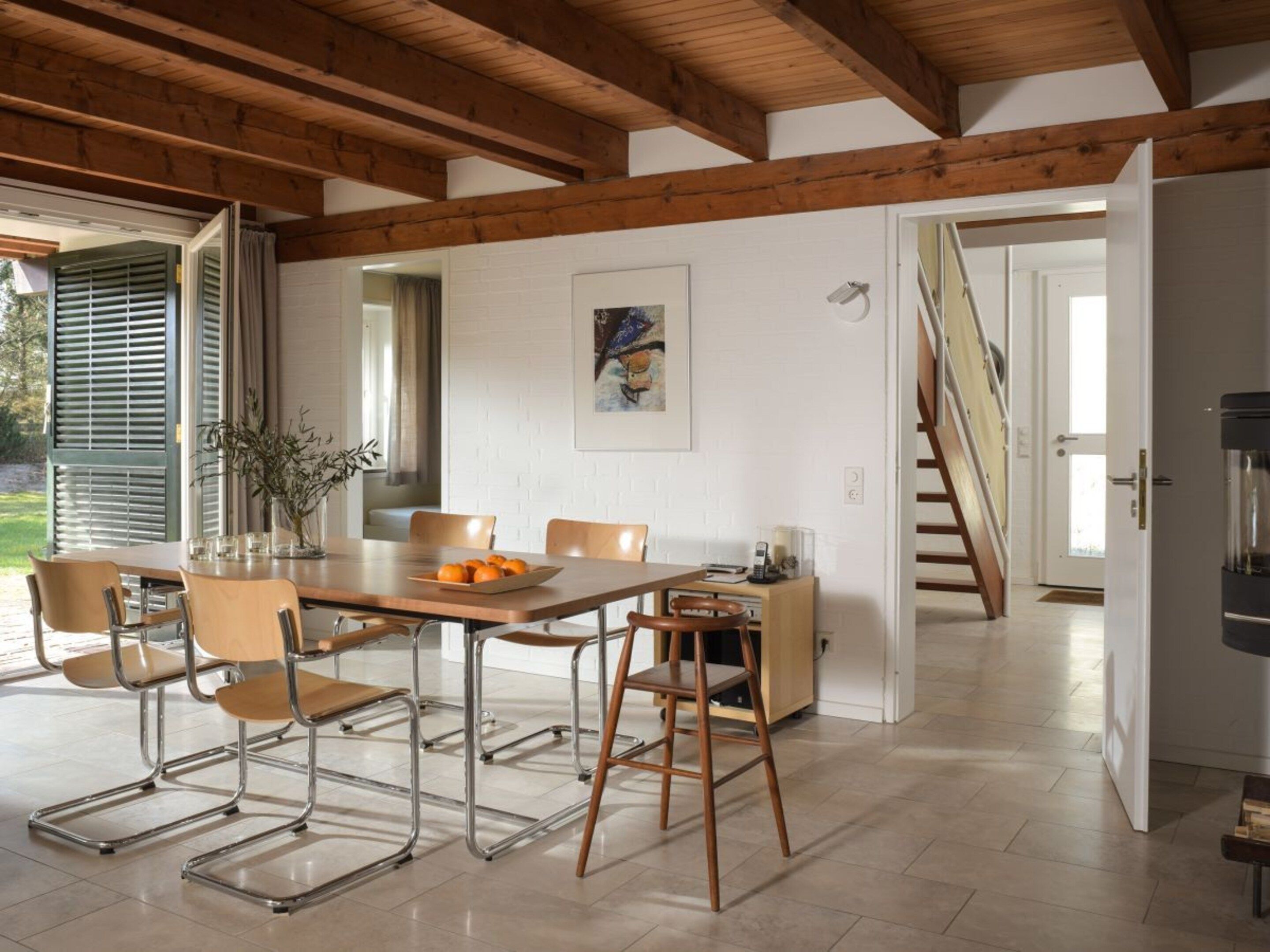 Uma sala de jantar com uma mesa e cadeiras de madeira, um quadro na parede e uma escada que leva a outro cômodo.