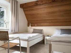 A bedroom with a sloped ceiling, a bed, a bedside table, a chair, and a window with curtains. - Holiday Home With 4 Bedrooms (St. Peter-Ording)