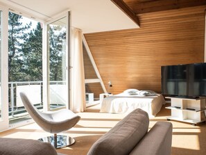A modern bedroom with a large bed, a television, and a balcony with a chair. - Holiday Home With 4 Bedrooms (St. Peter-Ording)