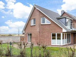 A two-story brick house with a sloped roof, large windows, and a balcony. - House Section "weitsicht" (St. Peter-Ording)