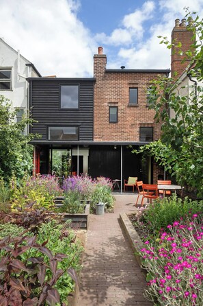 A modern house with a brick facade, a black extension, and a garden with various plants and flowers. - Historic Harwich Post Office w/Old Town Character (Essex)
